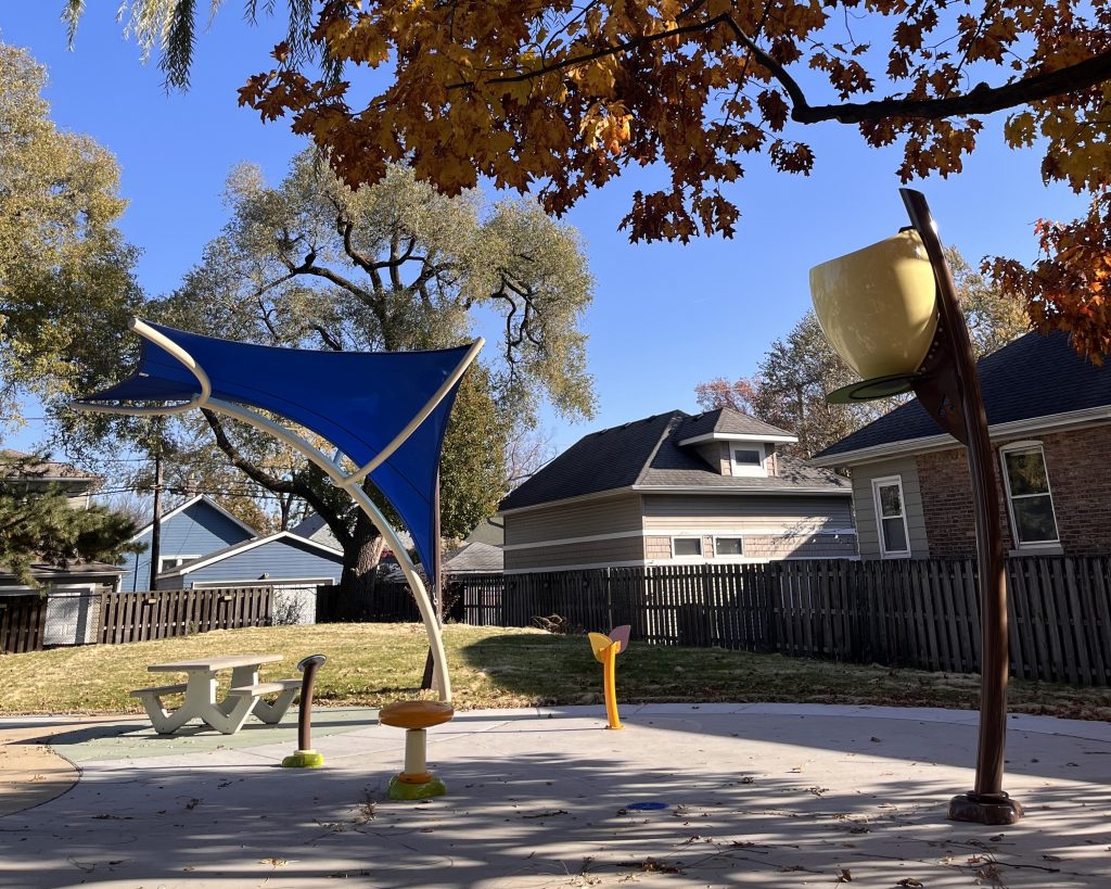 large blue shade structure over a concrete pad with dump bucket and other water spray features