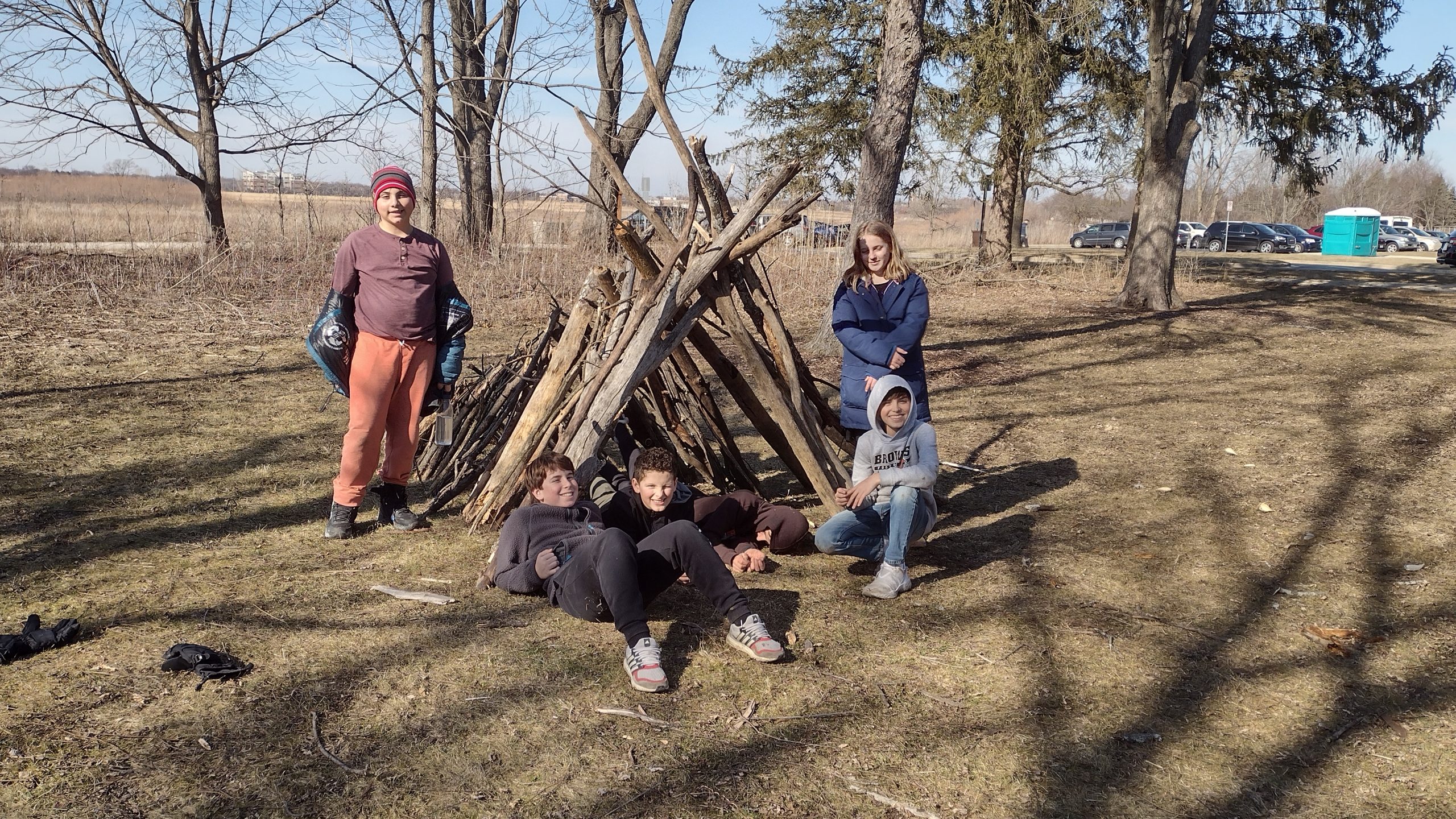 teens pose with a shelter made from branches
