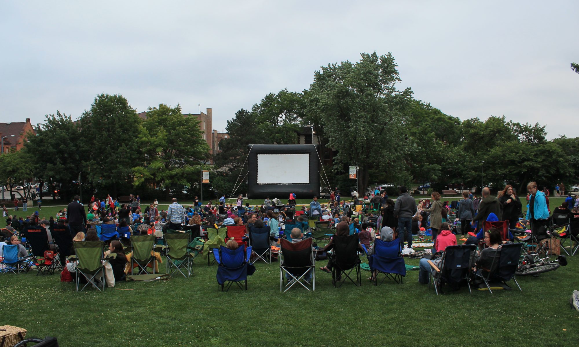 crowds sit in lawn chairs in front of a giant movie screen at scoville park