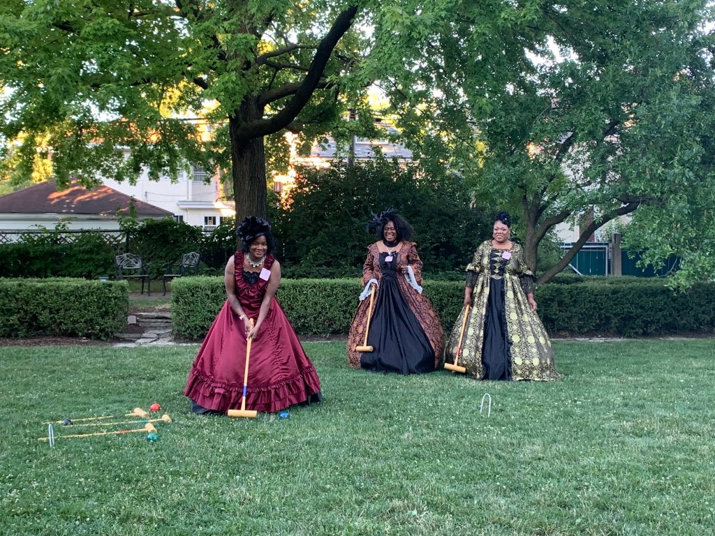 three women dressed in period gowns play croquet on the cheney lawn
