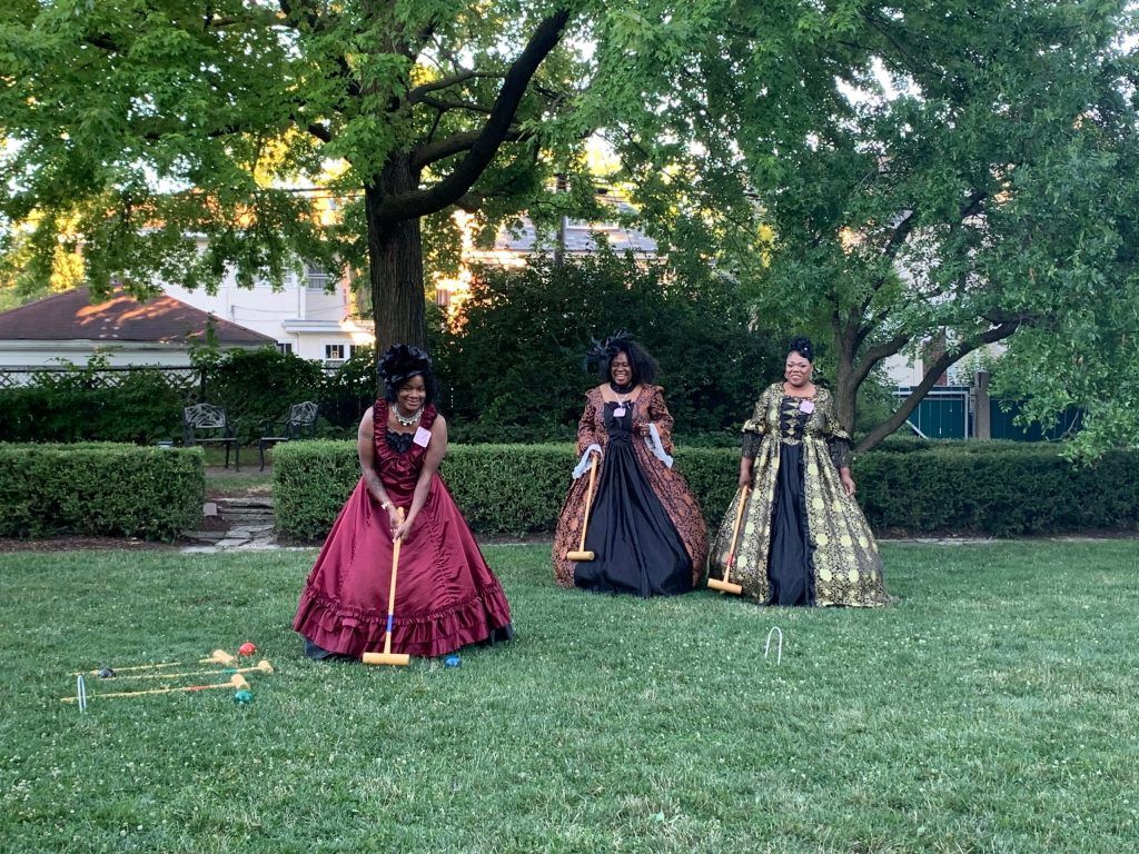 three women dressed in period gowns play croquet on the cheney lawn