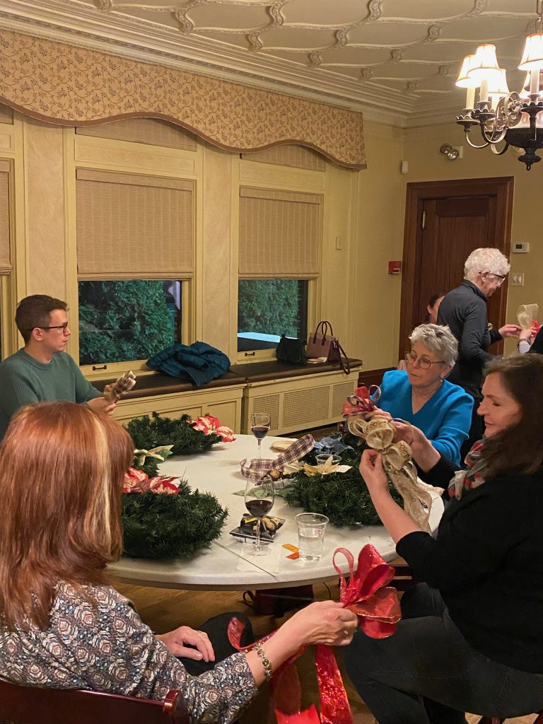 adults gather around a table to sip wine and make wreaths