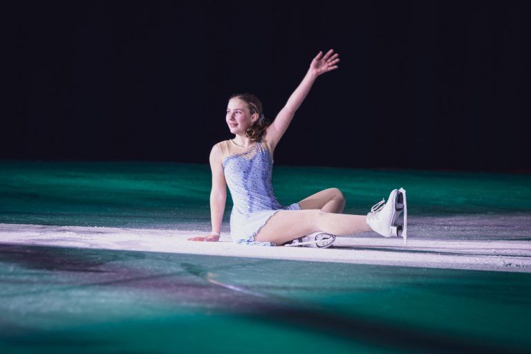 skater sits on ice in a pose wearing a sparkly purple costume