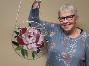 a woman holds up a stained glass depicting a peony