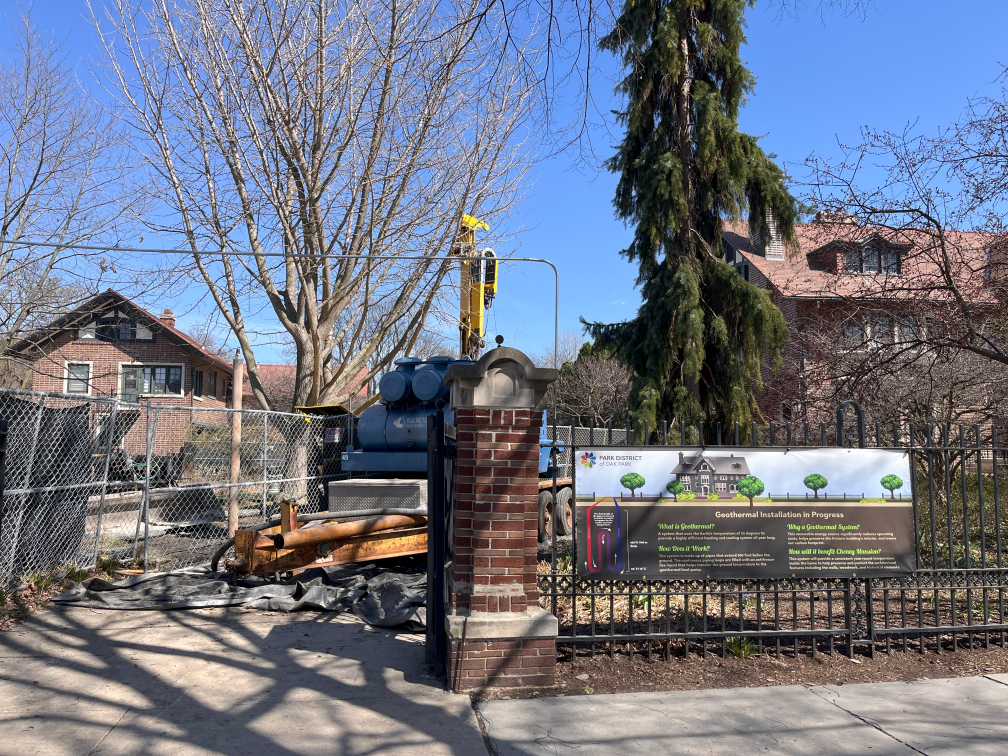 sign in front of cheney mansion announcing geothermal installation with machines in background