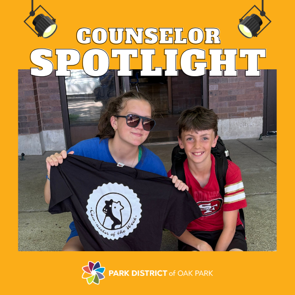 Annie holds up her counselor of the week tshirt and smiles next to one of her young campers