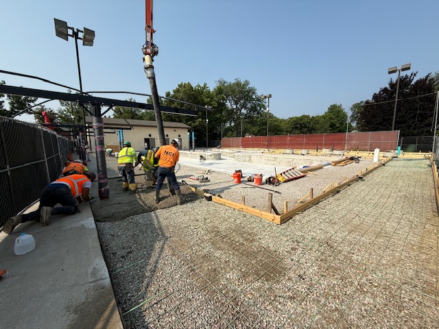 construction workers use a nozzle to pour concrete onto the gravel and rebar surface