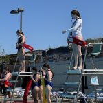 two lifeguards stand in their chairs and watch pool goers