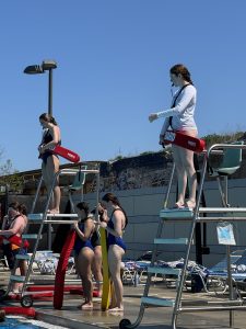 two lifeguards stand in their chairs and watch pool goers