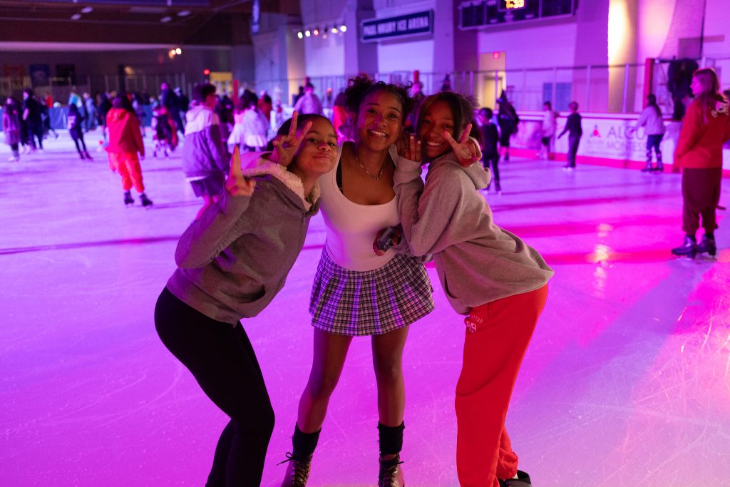 three girls hold up peace signs and hug on the rink