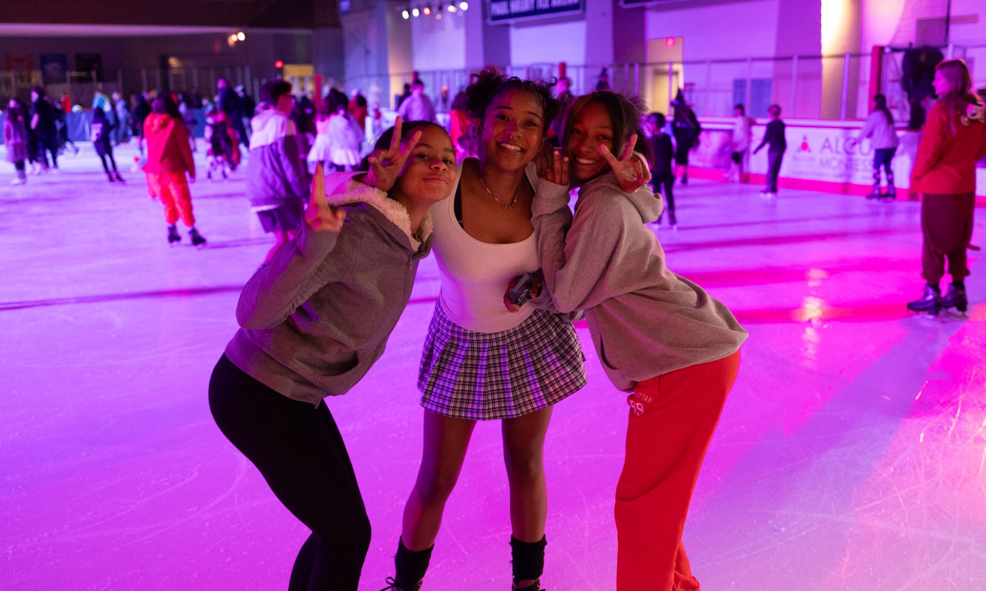 three girls hold up peace signs and hug on the rink