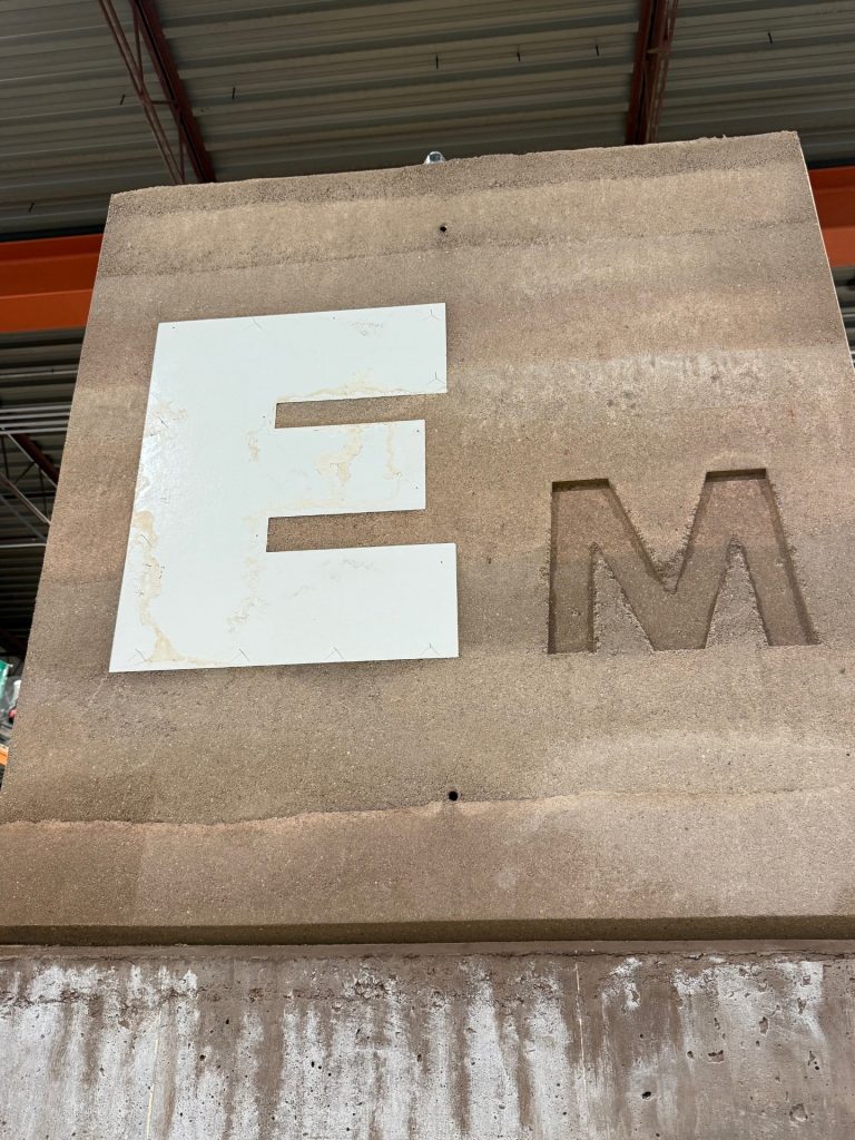large letter E and M pressed into brownish red rammed earth wall