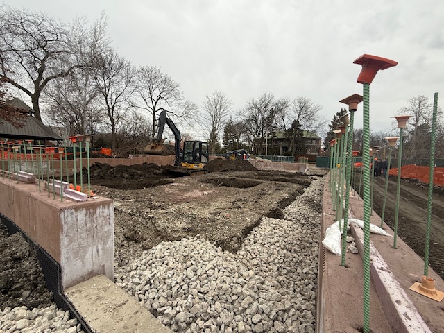 gravel surrounds concrete foundations with a backhoe in the distance