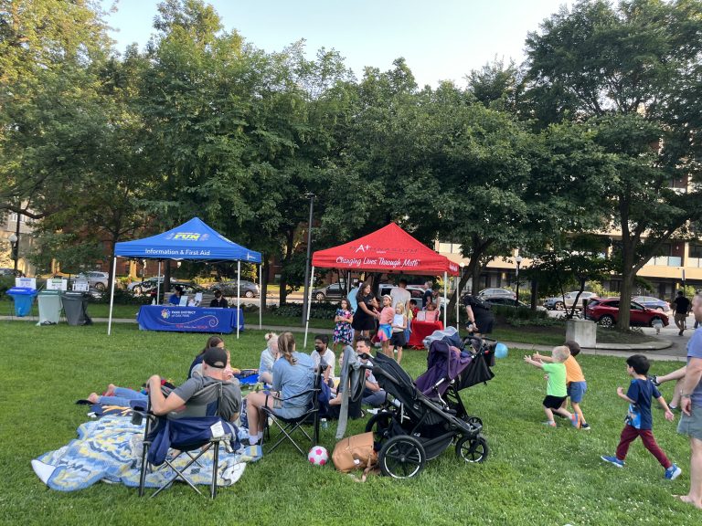 a family with small children sits in front of two tents on a grassy field