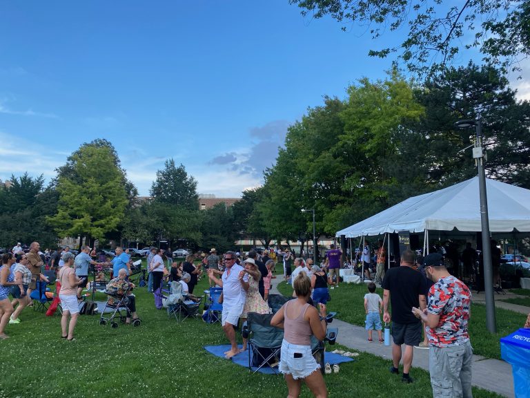large crowd of people stand in front of a tent in a park while dancing