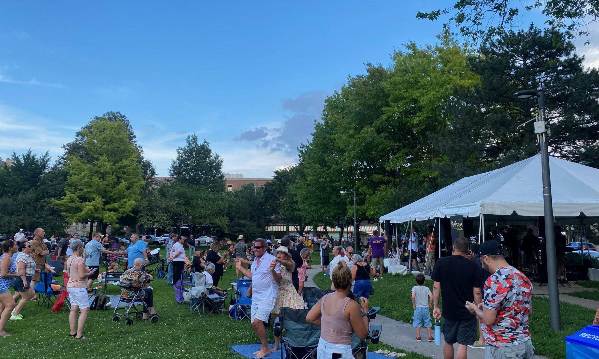 large crowd of people stand in front of a tent in a park while dancing