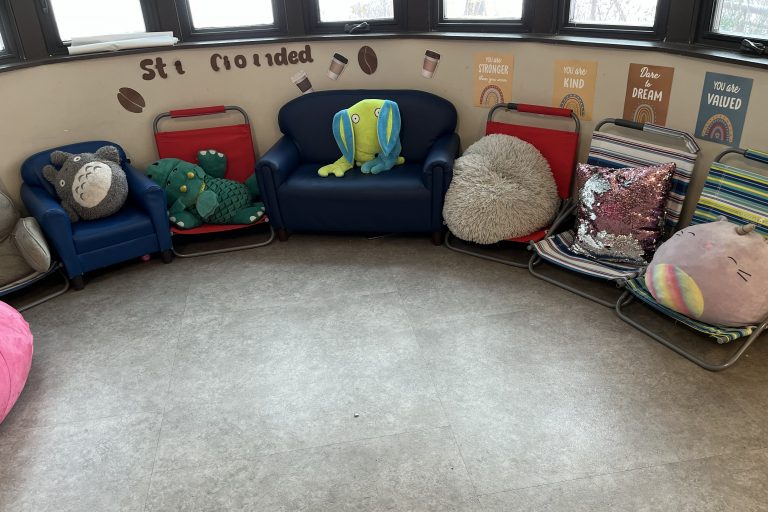 a cluster of plush chairs with pillows and stuffed animals and posters about reading