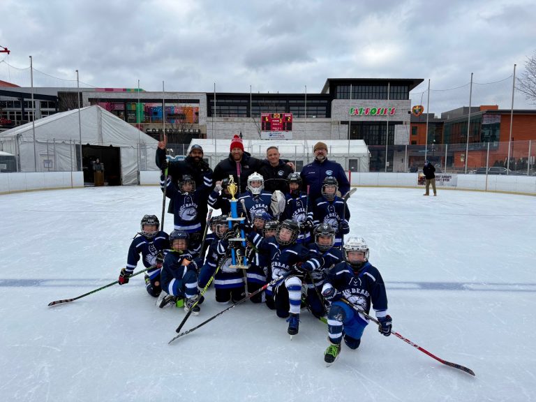 Ice bears in navy jerseys on outdoor ice rink with trophy