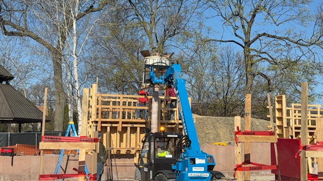 blue cherry picker truck sits next to framed out building