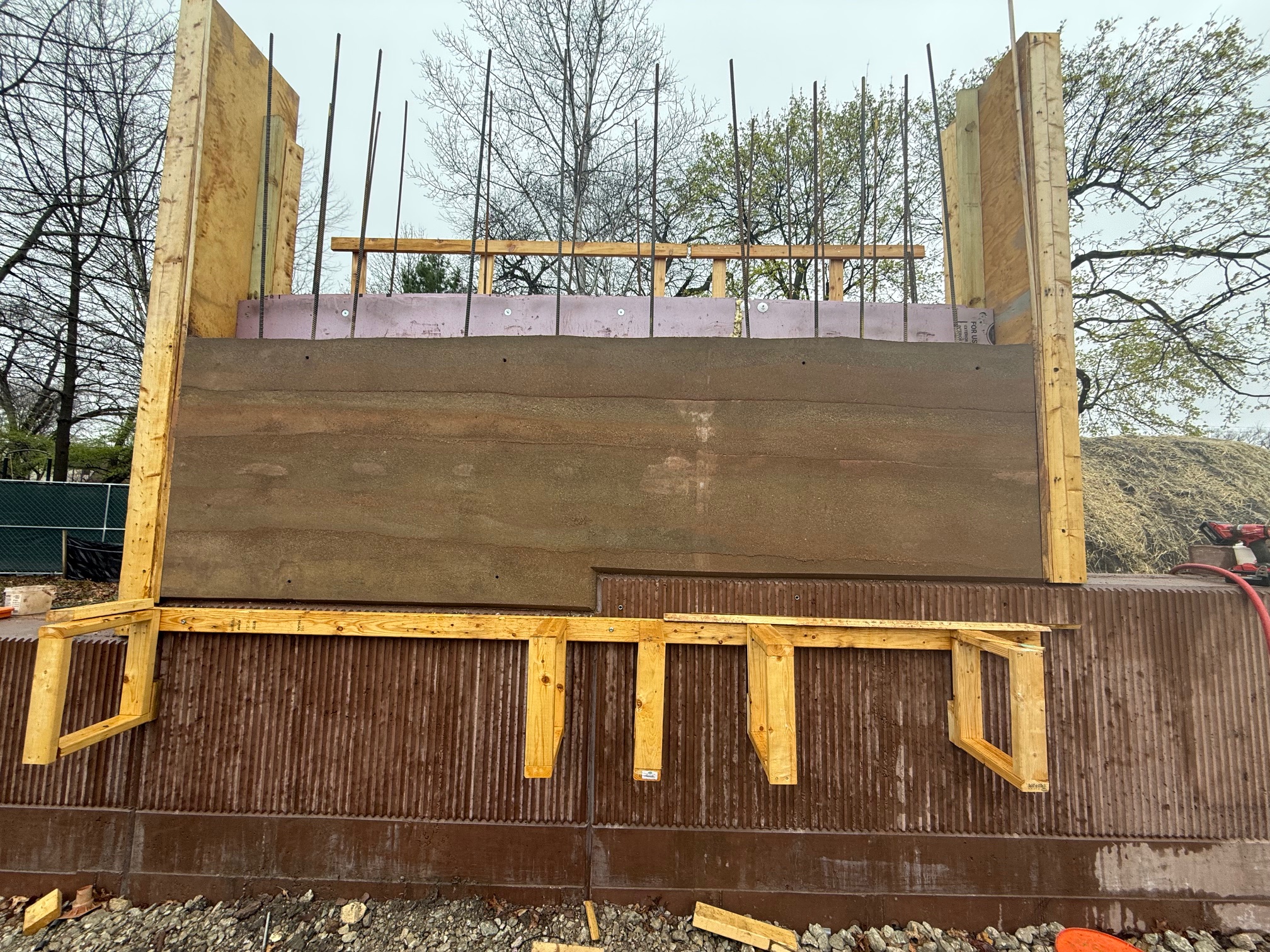 first rammed earth wall on the west side of the building, a brown clay looking wall between the plywood frames