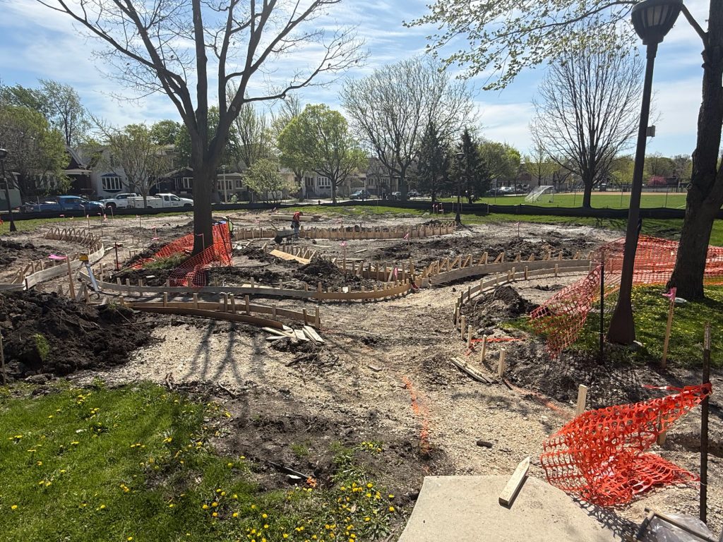 orange fencing surrounds a large dirt area with wood frames circling the perimeter