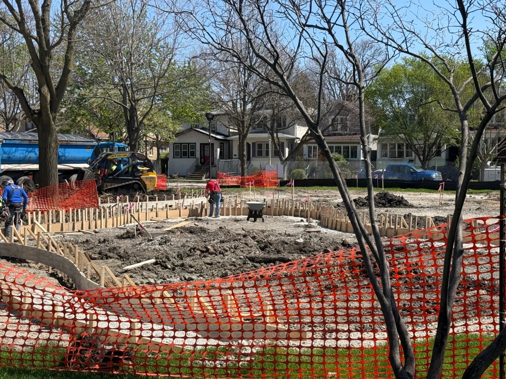 orange fencing surrounds a large dirt area with wood frames circling the perimeter