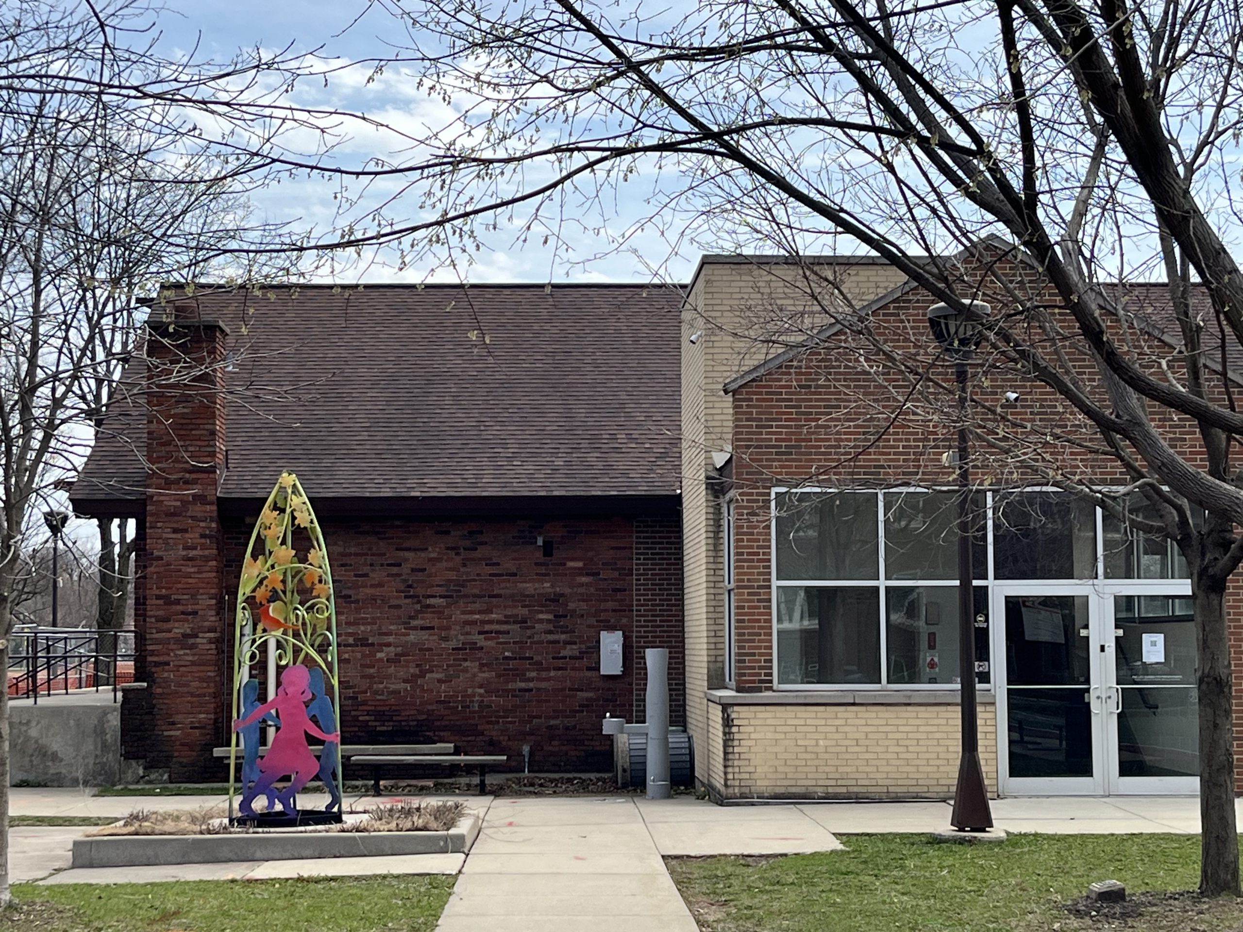 a ten foot tall steel sculpture depicting three children playing beneath a tree in pink, blue, green, and orange