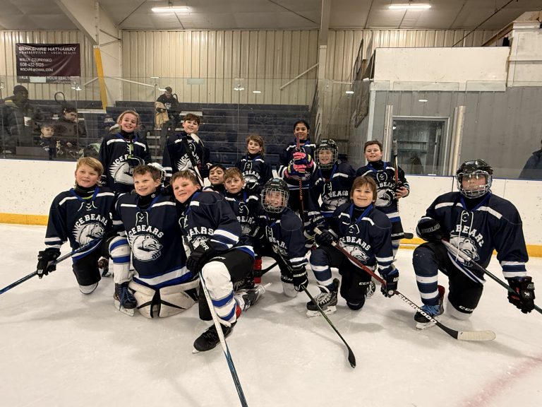ice bears in navy jerseys kneel on ice with their sticks