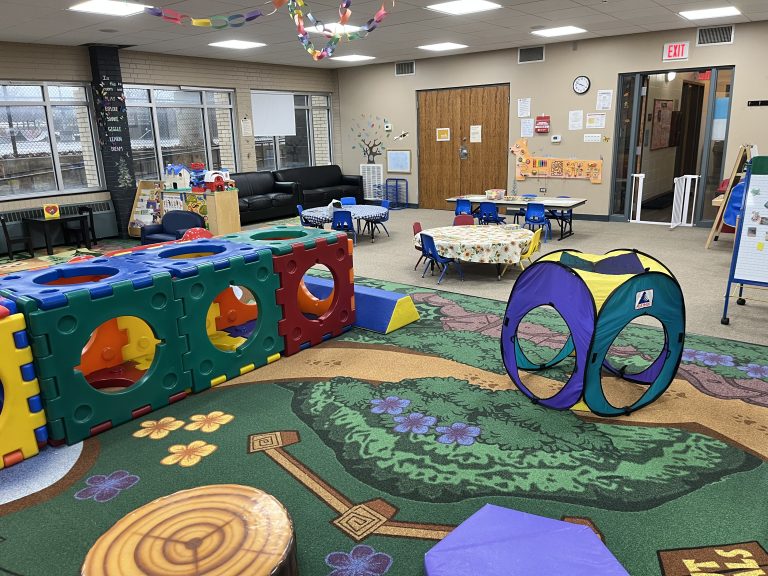 wide view of the cubhouse indoor playground with a nature themed rug, toddler tables, climbing equipment, and toys