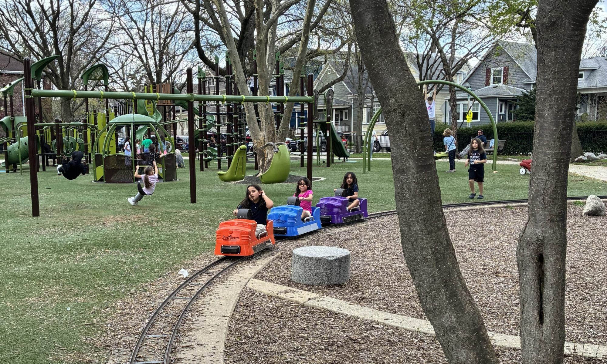 children sitting on orange, blue, and purple hand pedal train cars